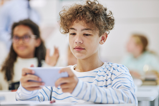 Minimal portrait of teen boy holding smartphone and playing mobile game in school