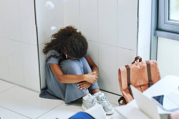 Depressed Black Girl in School High angle view of young black girl bullied in school and sitting on floor with headphones black girl scared stock pictures, royalty-free photos & images
