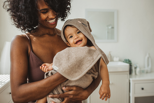 Smiling young mother wiping her baby with towel after having bath.