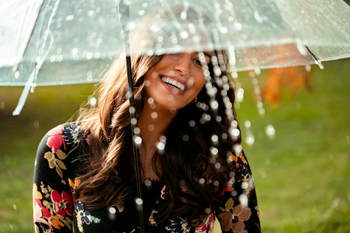 Pretty young woman smiling and holding umbrella while rain is falling, autumn portrait