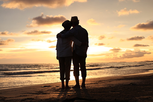Silhouette couple enjoy elderly relaxation on the beach against sunset or sunrise sky