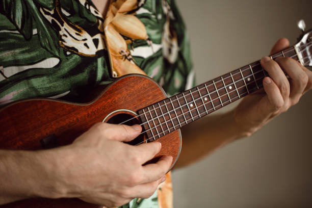 gray hair senior woman smiling and playing rhythmic music on a ukulele on the beach in front of the sea on a sunny day.retired hippie and bohemian woman enjoying her hobby.