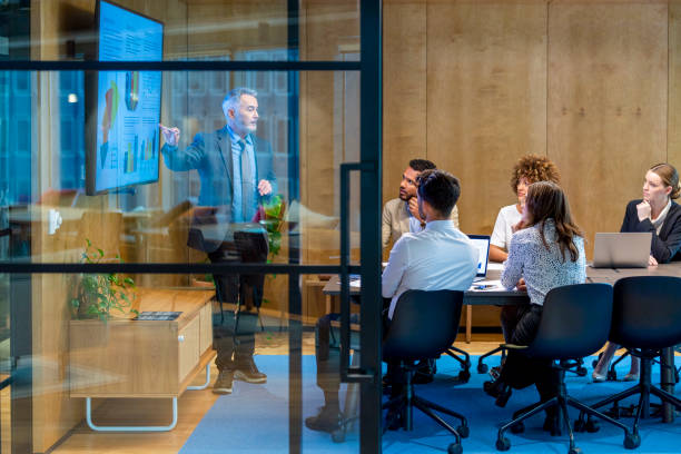 Mature man giving a big data presentation on a tv in a board room.