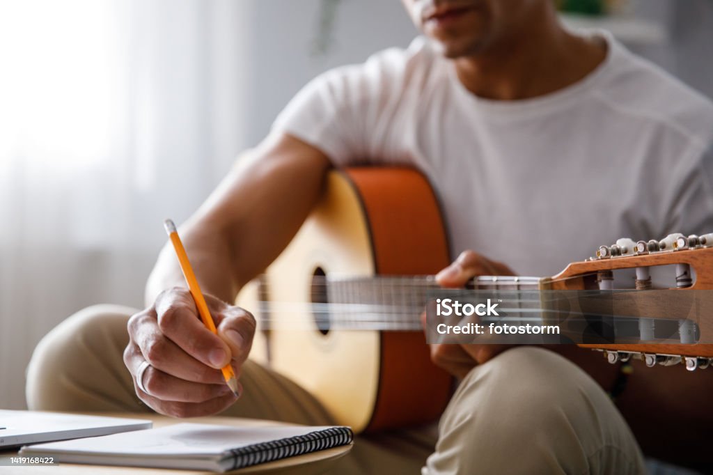 Man composing a song for acoustic guitar Man composing a song for acoustic guitar, writing chords in a notebook at home Composer Stock Photo