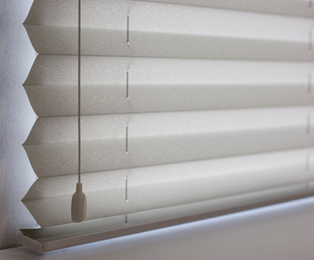 Pleated blinds white color close up, XL fold size, on the window in the interior. Premium home blinds, modern sun protection. Luxury window coverings.