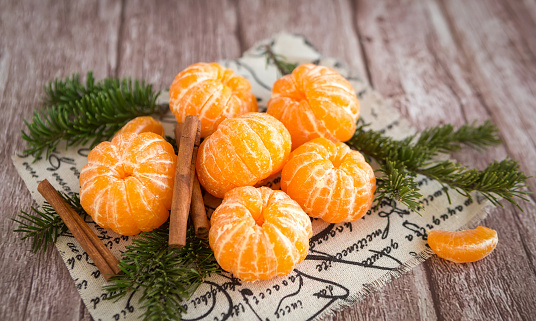 Orange mandarins or tangerines and cinnamon sticks on branches Christmas tree on brown wooden background. Selective focus. Christmas and New Year concept.