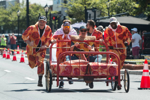 Men Wearing Pizza Costumes Compete In Charity Bed Race Event LAWRENCEVILLE, GA / USA - APRIL 23:  Men wearing pepperoni pizza costumes push a bed down the street in a charity bed race event on April 23, 2022 in Lawrenceville, GA.. struggle photos stock pictures, royalty-free photos & images