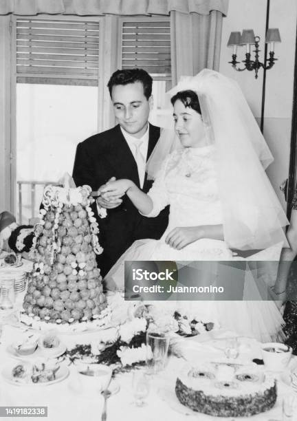 Vintage Image From The 50s Young Couple Posing Cutting Their Wedding Cake Stock Photo - Download Image Now