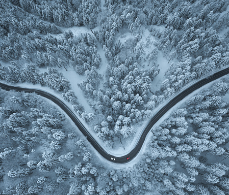 Aerial view on the road leading through snowcapped winter forest. Three cars driving on the road.