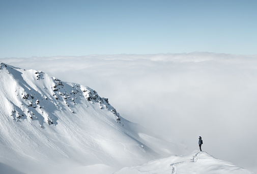 Woman standing on the edge of the snowcapped mountain above the fog enjoying the view.