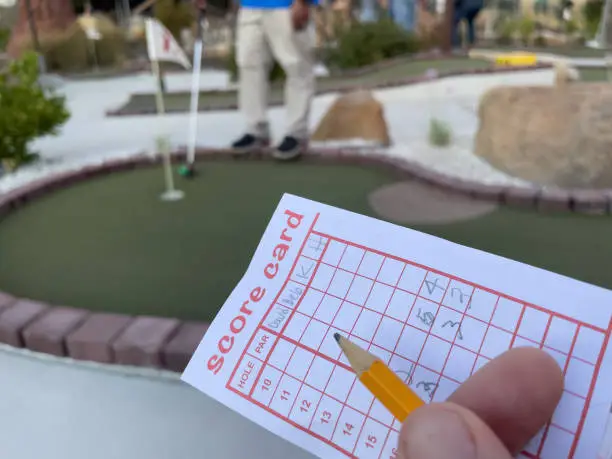 human fingers holding on to pencil and golf score card at mini golf course