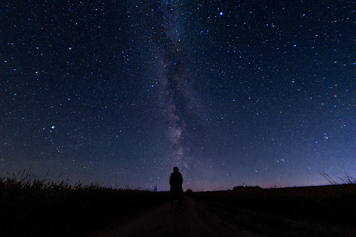 abstract night photo of a figure of a lonely person in a field under a starry sky and northern lights, starfall. Astrophotography