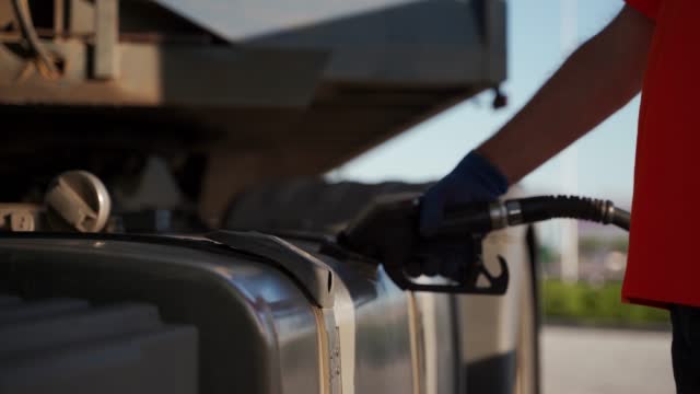 Truck driver refuels a fuel tank with diesel filling gun intruck at petrol station. Concept of increasing soaring fuel prices, economical problems. Trucker man refilling the motor lorry.
