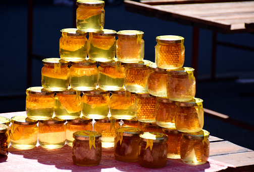 golden color honey jars in bright sunlight on display in open market place. small glass containers with metal lids, shiny and reflective with shadow. food concept. wooden table. organic origin concept