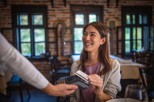 Photo of smiling  asian woman paying with credit card in restaurant