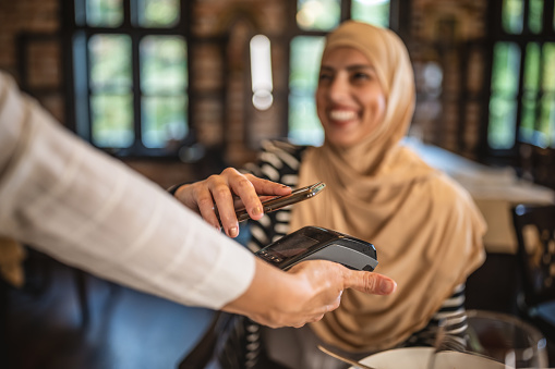 Photo of smiling muslim woman paying with credit card in restaurant