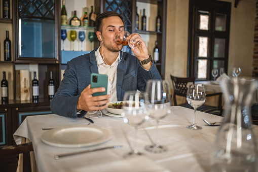 Photo of businessman sitting in restaurant and having online call by mobile phone.