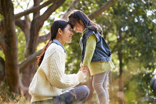 young asian mother and preschool daughter enjoying nature having a good time outdoors in park