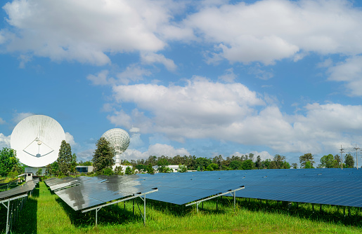 Solar farm and green field with blue sky. Big satellite dish near solar farm. Solar power for green energy. Photovoltaic power plants generate solar energy. Renewable energy. Sun power for commercial.