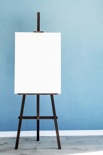 Wooden easel with blank canvas on light blue wall background for mockup design. Space for text