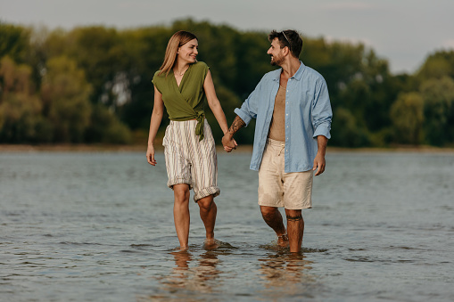 Beautiful and attractive couple walking through the water, while at the beach, enjoying talking and holding hands, smiling. Radiating love. Vacation, beach , romance, concept