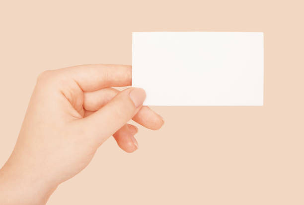 istock Female hand holding white blank paper sheet mockup on beige background. 1419240593