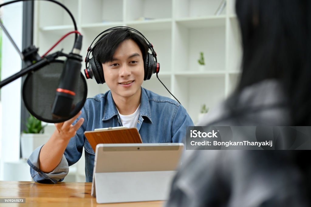 Talented asian male radio host enjoy discussing and interviewing his female special guest Professional and talented young asian male radio host enjoy discussing and interviewing his female special guest during the podcast show in the studio. Happiness Stock Photo