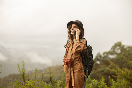 Smiling young woman in hat with backpack talking on mobile phone, copy space