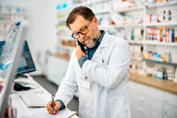 Photo of Pharmacist taking notes while talking on the phone in a pharmacy.