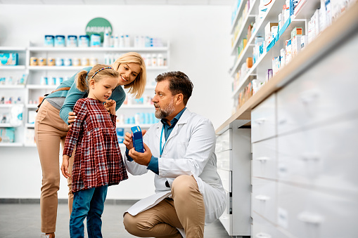 Mature pharmacist talking to a little girl and her mother while assisting them in buying a medicine in pharmacy.