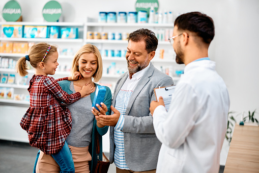 Happy parents with their daughter buying medicine while pharmacist is assisting them in drugstore.