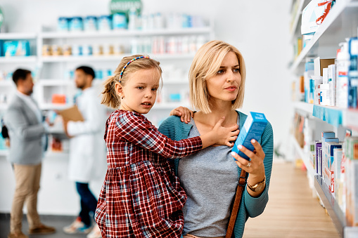 Uncertain mid adult woman choosing products while being with her daughter in a pharmacy.