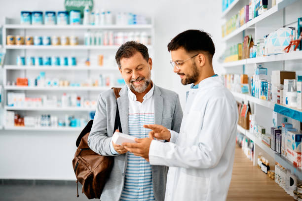 Happy man choosing medicine with help of young pharmacist in drugstore. Young pharmacist talking to male customer in a drugstore. Focus is on customer. pharmacist stock pictures, royalty-free photos & images