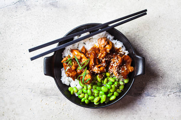 Teriyaki chicken with rice , onion and edamame beans in black bowl. Teriyaki chicken with rice , onion and edamame beans in a black bowl, top view. Japanese cuisine. sticky sesame chicken sauces stock pictures, royalty-free photos & images