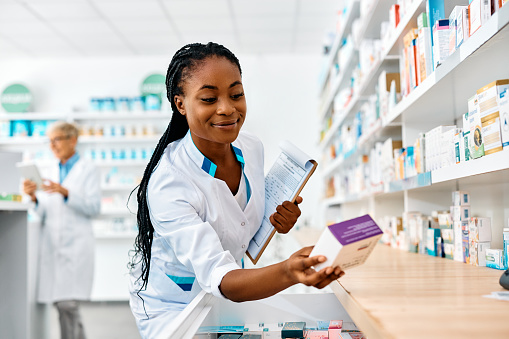 Happy African American female pharmacist looking for medicine while working in drugstore.