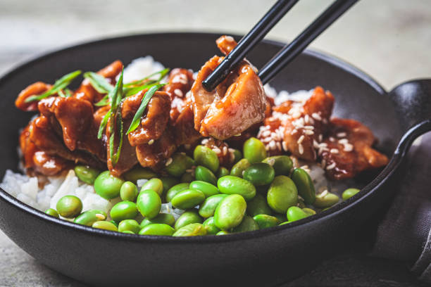 Teriyaki chicken with rice , onion and edamame beans in black bowl. Teriyaki chicken with rice , onion and edamame beans in a black bowl, close-up. Japanese cuisine. sticky sesame chicken sauces stock pictures, royalty-free photos & images