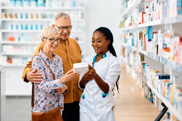 felice farmacista donna nera che assiste la coppia di anziani nella scelta della medicina in una farmacia. - farmacista foto e immagini stock