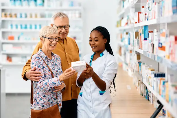 Happy African American pharmacist advising senior couple in choosing vitamins in drugstore.