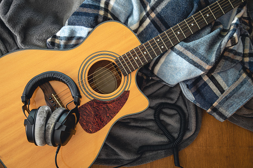 Acoustic guitar, plaids and and headphones on a wooden background, top view, the concept of musical creativity.