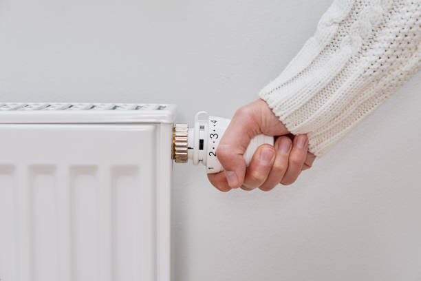 femme en pull chaud réglant la température sur le radiateur chauffant - room temperature photos et images de collection