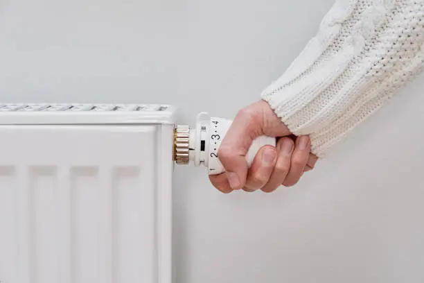 Photo of Woman in warm sweater adjusting temperature on heating radiator