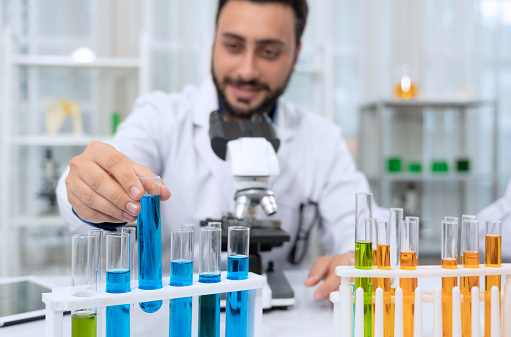 Scientist wearing white laboratory coat in reserch laboratory. Man holding test tube with blue reagent and using microscope