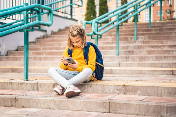 istock Back to elementary, primary school. Little girl with backpack,mobile phone. Chat, talk with friends, classmates on break. Autumn study after vacation. Education of children. Pupil kid on stair steps 1419255992