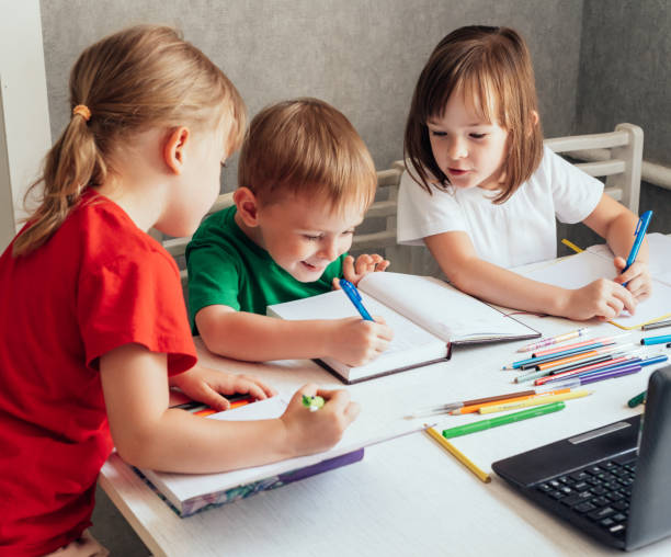 istock Children sit at a table with pens and notebooks and use a laptop 1419257299