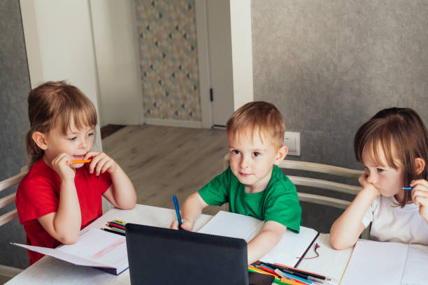istock Children sit at a table with pens and notebooks and use a laptop 1419257358