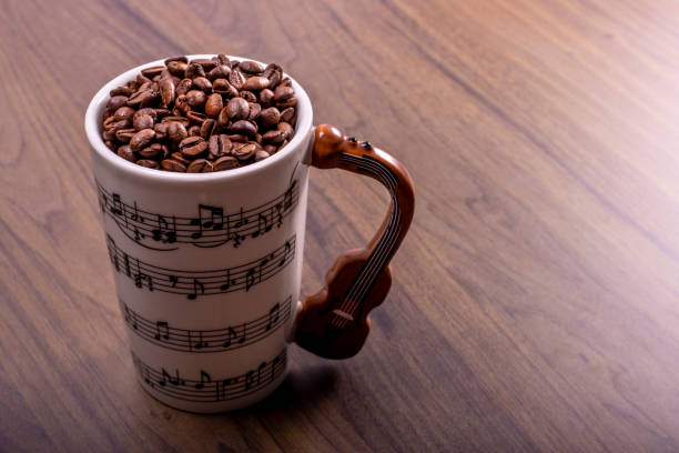 istock Natural coffee beans in an artistic musical cup. Music notes painted on the cup with a cello shaped handle. International Coffee Day concept. October 1st. 1419257461