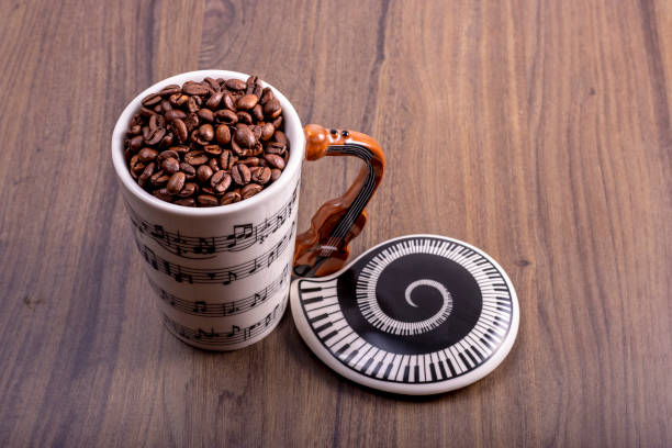 istock Natural coffee beans in an artistic musical cup. Music notes painted on the cup with a cello shaped handle and a plate with piano keys. International Coffee Day concept. October 1st. 1419257475