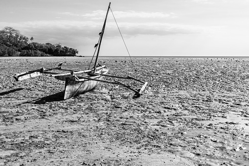 canoe beached on the mud flats of the outgoing tide in black and white.