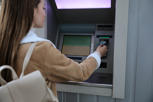 Young woman using cash machine for money withdrawal outdoors, focus on hand