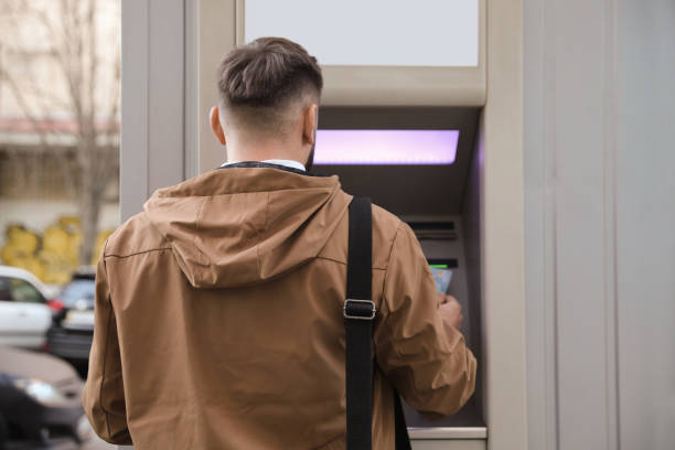 istock Young man using cash machine for money withdrawal outdoors, back view 1419266939